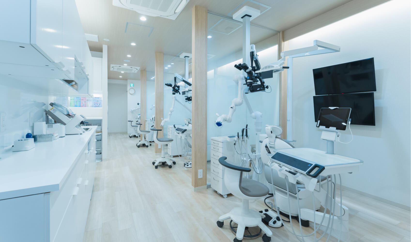 清潔感のある歯科医院の一般治療エリア。プライバシーに配慮された治療ユニットが複数並んでいる。