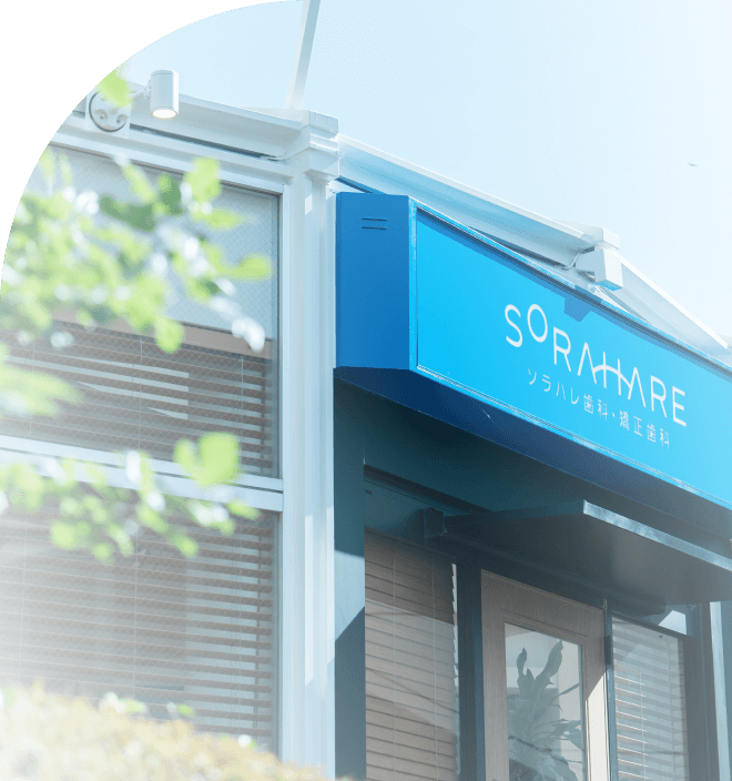 東大和市・玉川上水駅から徒歩1分にあるソラハレ歯科・矯正歯科の外観。晴れた空の下、緑の木々の隣に立つモダンでクリーンな建物。