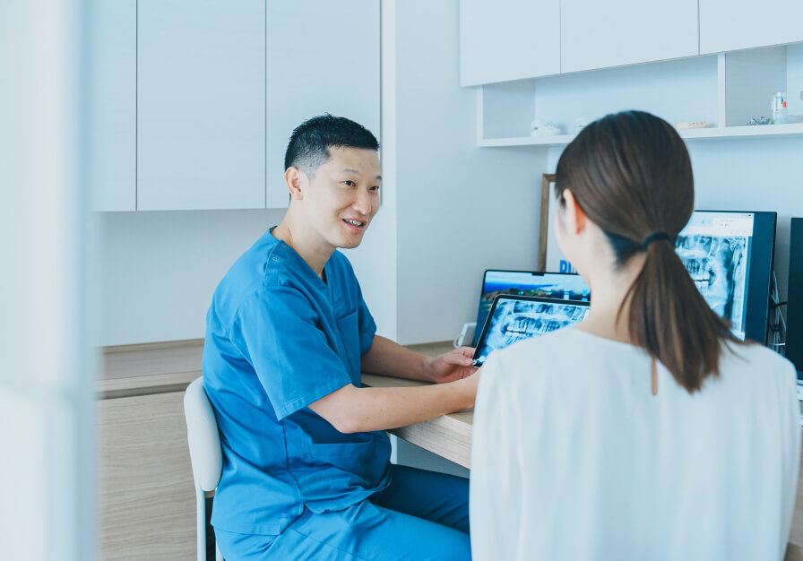 パソコンの画面データを見ながら、インプラント治療の準備について説明する歯科医師