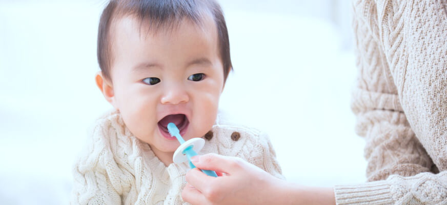 0歳からの虫歯予防のために、お母さんが赤ちゃんの歯を優しく磨いている